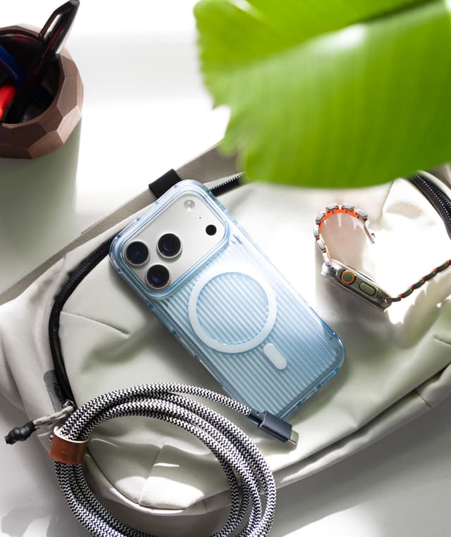 Nimbus9 Alto 2 Clear case in Clear Blue on an iPhone, resting on a canvas bag beside an Apple Watch, braided cable, and a leaf