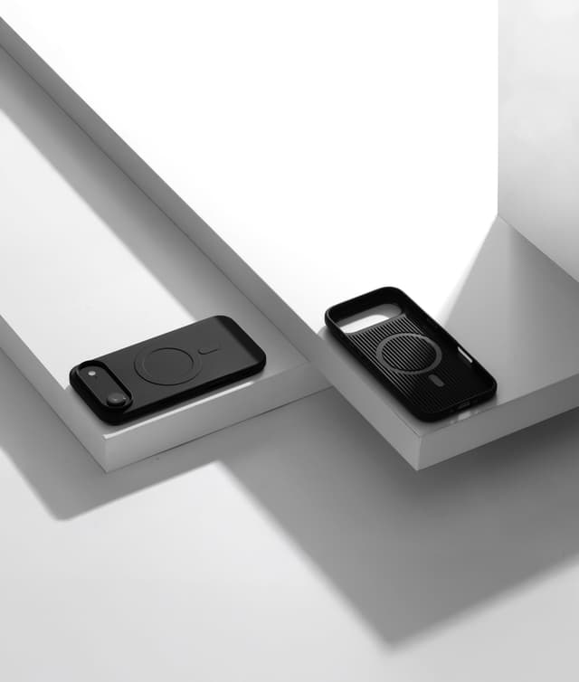 Two Nimbus9 Alto 2 cases in Black on white plinths — one on a phone showing the camera cutout, one empty with its MagSafe ring visible