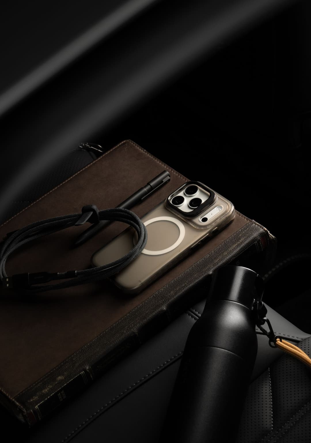 Stratus 2 case on a phone lying on a leather notebook in a car beside a coiled cable and a tumbler