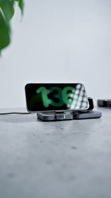 A phone lying sideways on the standing magnetic pad showing a large clock, a watch charging on the pad beside it