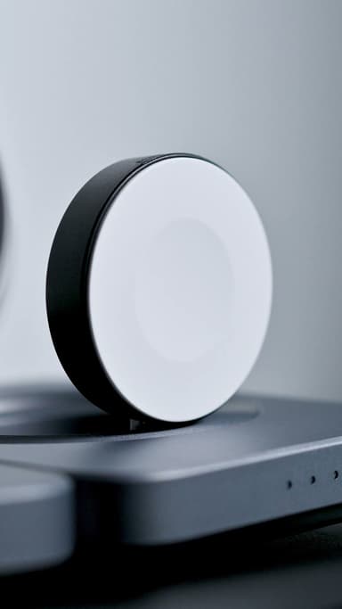 Close view of the station's round watch charger standing on its hinge above the base, its pale charging face turned to the camera