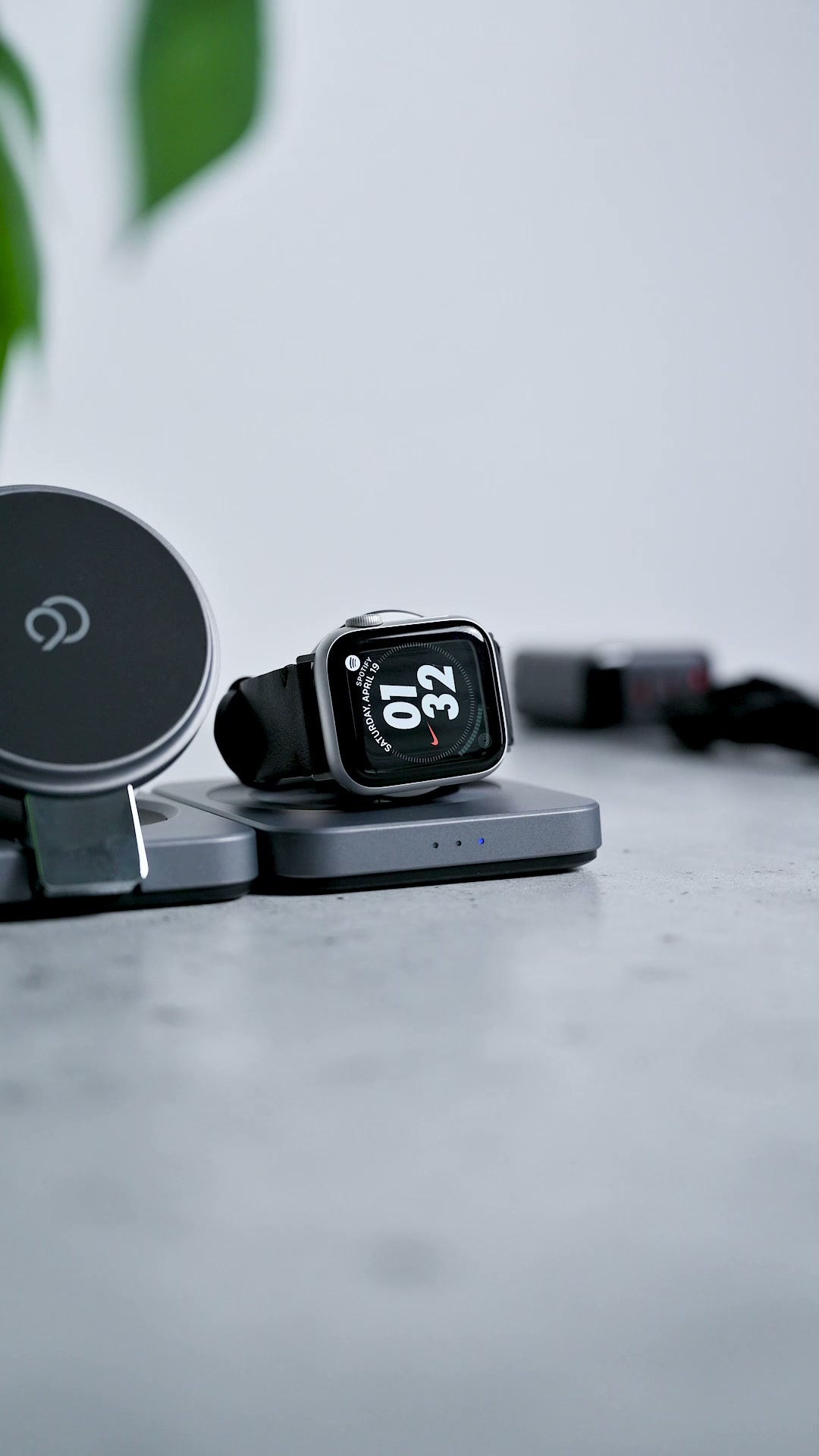 A watch resting on the station's round dock showing the time, the magnetic phone pad standing beside it and three status lights on the base