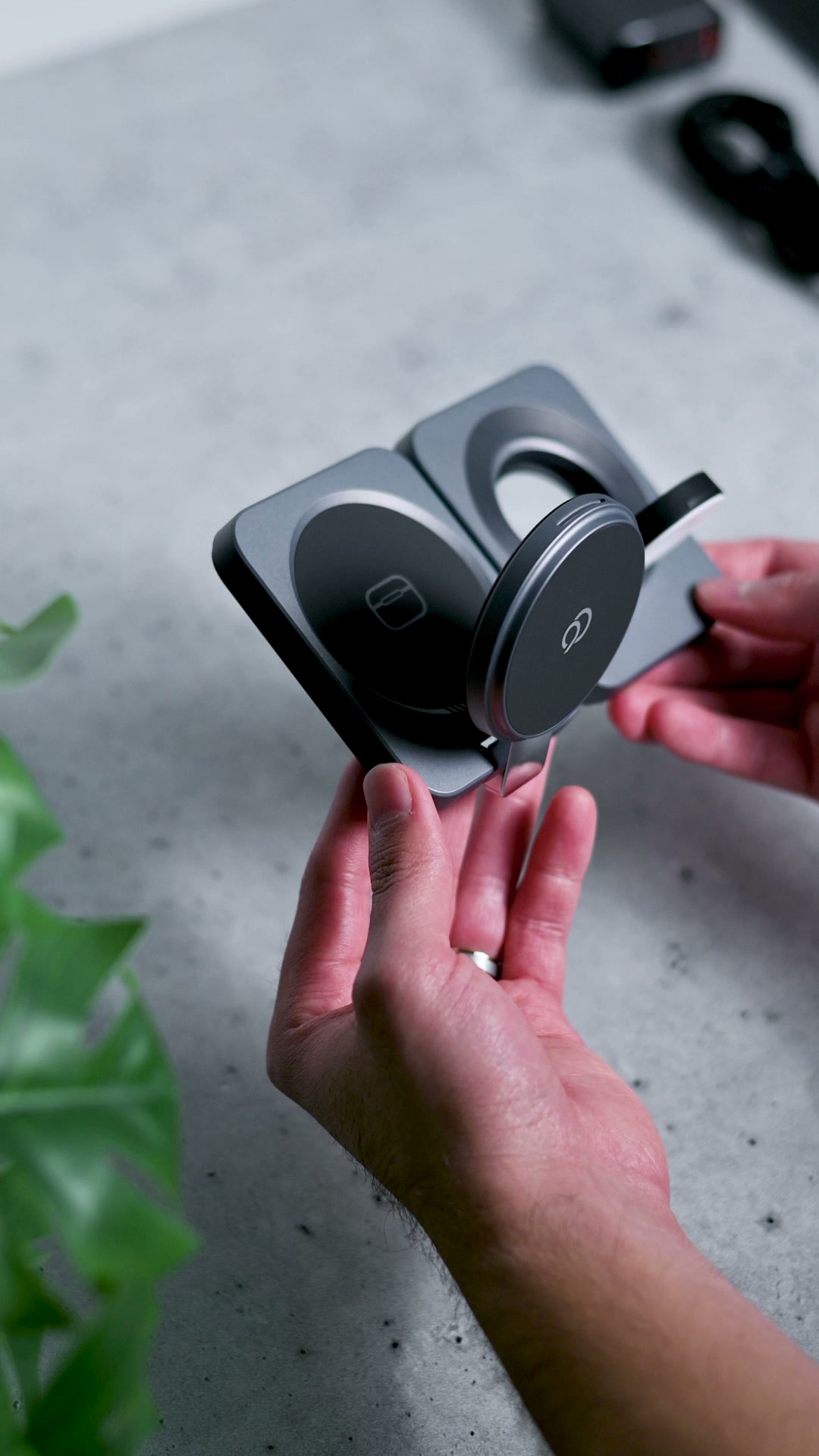 Two hands opening the charging station, the round watch charger swinging out of the second panel on its hinge