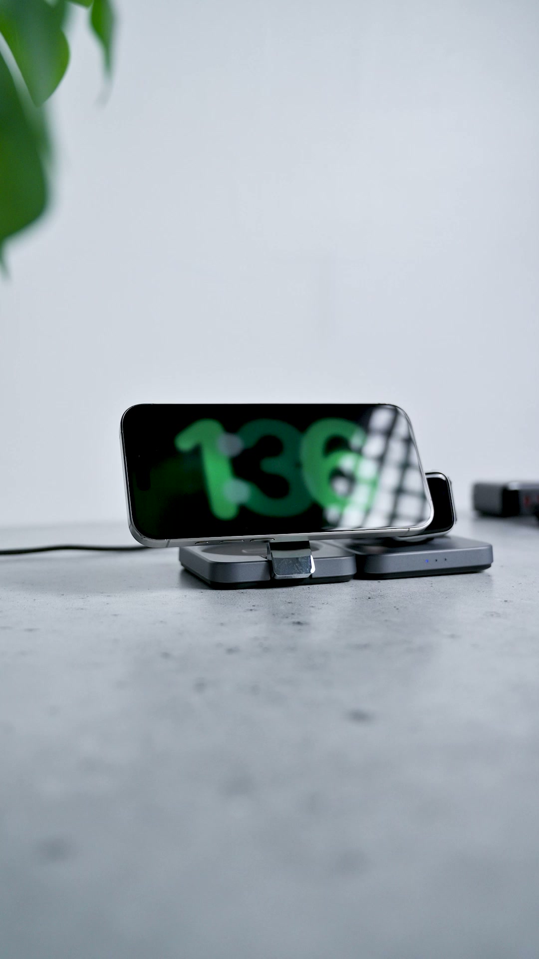 A phone lying sideways on the standing magnetic pad showing a large clock, a watch charging on the pad beside it
