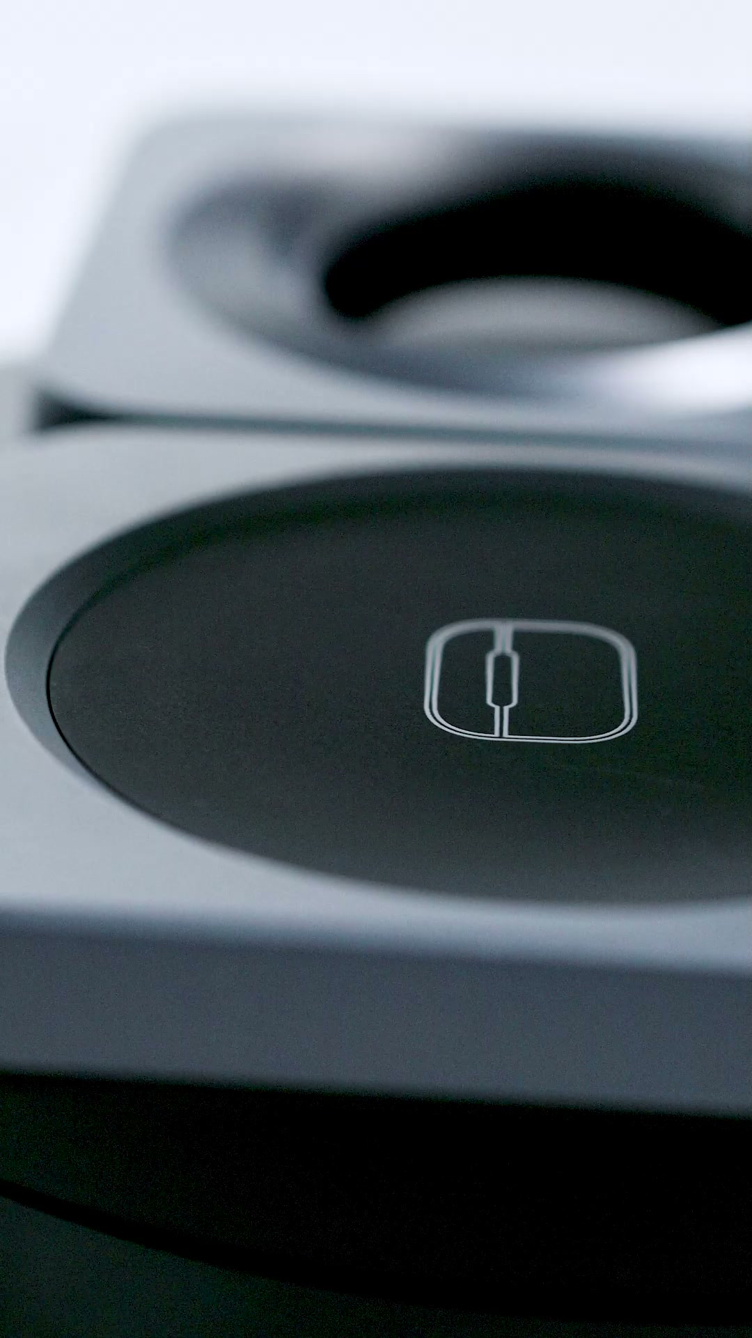 Close view of the station's flat charging pad, a small etched icon at its center, the watch cradle out of focus behind it