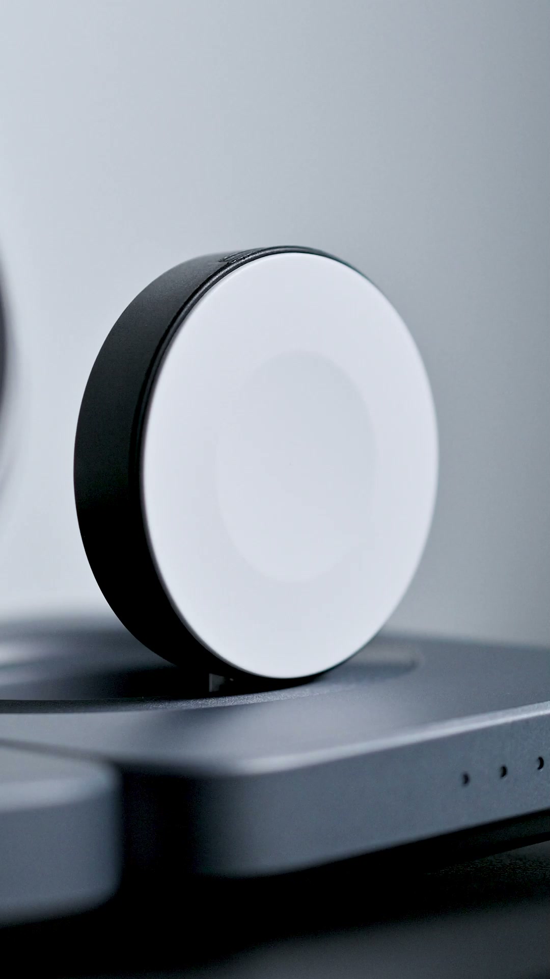 Close view of the station's round watch charger standing on its hinge above the base, its pale charging face turned to the camera
